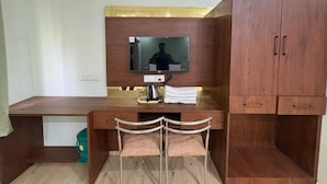 Una habitación con un escritorio de madera, dos sillas, un televisor montado en la pared y un armario.