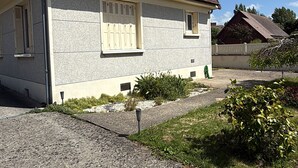 Una casa a due piani con tetto spiovente, una finestra con persiane e un piccolo giardino con piante e un vialetto ghiaioso.