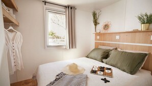 Ein Schlafzimmer mit einem Bett, einem Fenster, einem Regal mit Pflanzen und einer Kleiderstange.