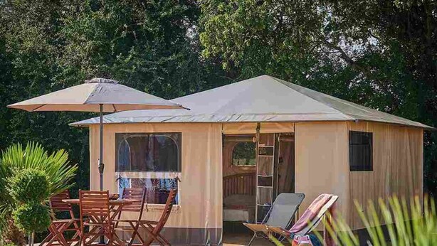 Eine kleine, einstöckige Holzhütte mit einer überdachten Terrasse, einem Tisch, Stühlen und einer Leiter, die zu einer oberen Ebene führt.