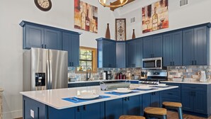 A modern kitchen with blue cabinets, stainless steel appliances, and a large island with stools. - Terracotta Retreat · Sleeps 54 · Pool & Hot Tub (Wimberley)