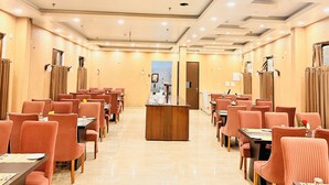 A hotel dining area with rows of tables and chairs, a reception desk, and a view of the lobby.