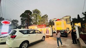 A hotel entrance with a sign for 'Hotel Red Sapphire,' a white car parked in front, and a person standing near the entrance.