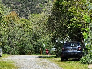 A gravel road leading to a parked car surrounded by dense greenery and trees. - Mobile home with AC - 4 guests (Arles-sur-Tech)
