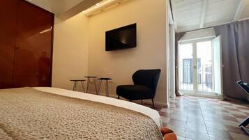 A hotel room with a bed, a TV mounted on the wall, a chair, a small table, and a balcony with a view.