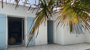 A building with a tiled patio, a door with a blue interior, and a palm tree. - Family house with indoor courtyard - 4 guests (Noirmoutier-en-l'Île)