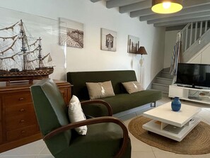 Ein Wohnzimmer mit einem grünen Sofa, einem Holzstuhl, einem Couchtisch, einem Fernseher und einem Schiffmodell.
