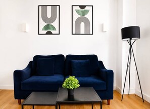 Ein Wohnzimmer mit einem dunkelblauen Sofa, einem kleinen Tisch mit einer Pflanze und zwei abstrakten Wandbildern.