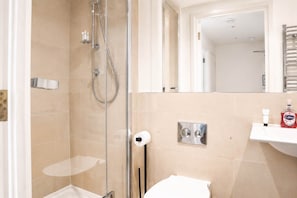A bathroom with a glass-enclosed shower, a toilet, a sink with a soap dispenser, and a mirror above the sink. - Charming 1BR with Balcony in Central Fitzrovia (London)
