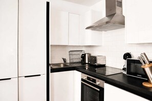 A modern kitchen with white cabinets, a black countertop, a stainless steel range hood, a toaster, a coffee maker, a microwave, and a knife block. - Charming 1BR with Balcony in Central Fitzrovia (London)