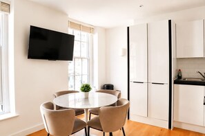 A modern kitchen with white cabinets, a black countertop, and a built-in TV. - Charming 1BR with Balcony in Central Fitzrovia (London)