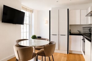 A modern kitchen with white cabinets, a black countertop, and a flat-screen TV mounted above the dining table. - Charming 1BR with Balcony in Central Fitzrovia (London)