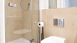Eine begehbare Dusche mit Glastrennwand, eine Handbrause, eine Toilette und ein Handtuchspender.