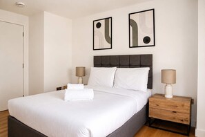A neatly made bed with white linens, two bedside tables with lamps, and abstract artwork on the wall. - Fitzrovia and West End Residences (London)