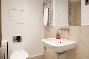 A bathroom with a white sink, a toilet, a towel rack, and a mirror. - Fitzrovia and West End Residences (London)
