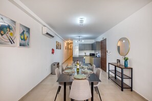 Ein Essbereich mit Tisch für vier Personen, eine Küche im Hintergrund und ein Spiegel an der Wand.