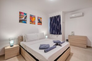 Ein modernes Schlafzimmer mit Bett, Nachttischen, einem Schminktisch und Kunstwerken an der Wand.