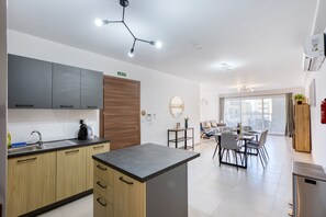 A modern kitchen with a central island, built-in cabinets, and a dining area with a table and chairs. - Bright & luxury apartment with 2 balconies JVEL1-1 (St. Paul’s Bay)