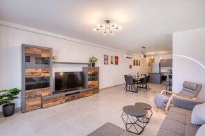 Ein modernes Wohnzimmer mit Flachbildfernseher, einem Essbereich und einer Küche im Hintergrund.
