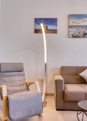 Ein modernes Wohnzimmer mit einem grauen Sofa, einem Holzsesseln, einer Stehlampe und zwei Wandbildern.