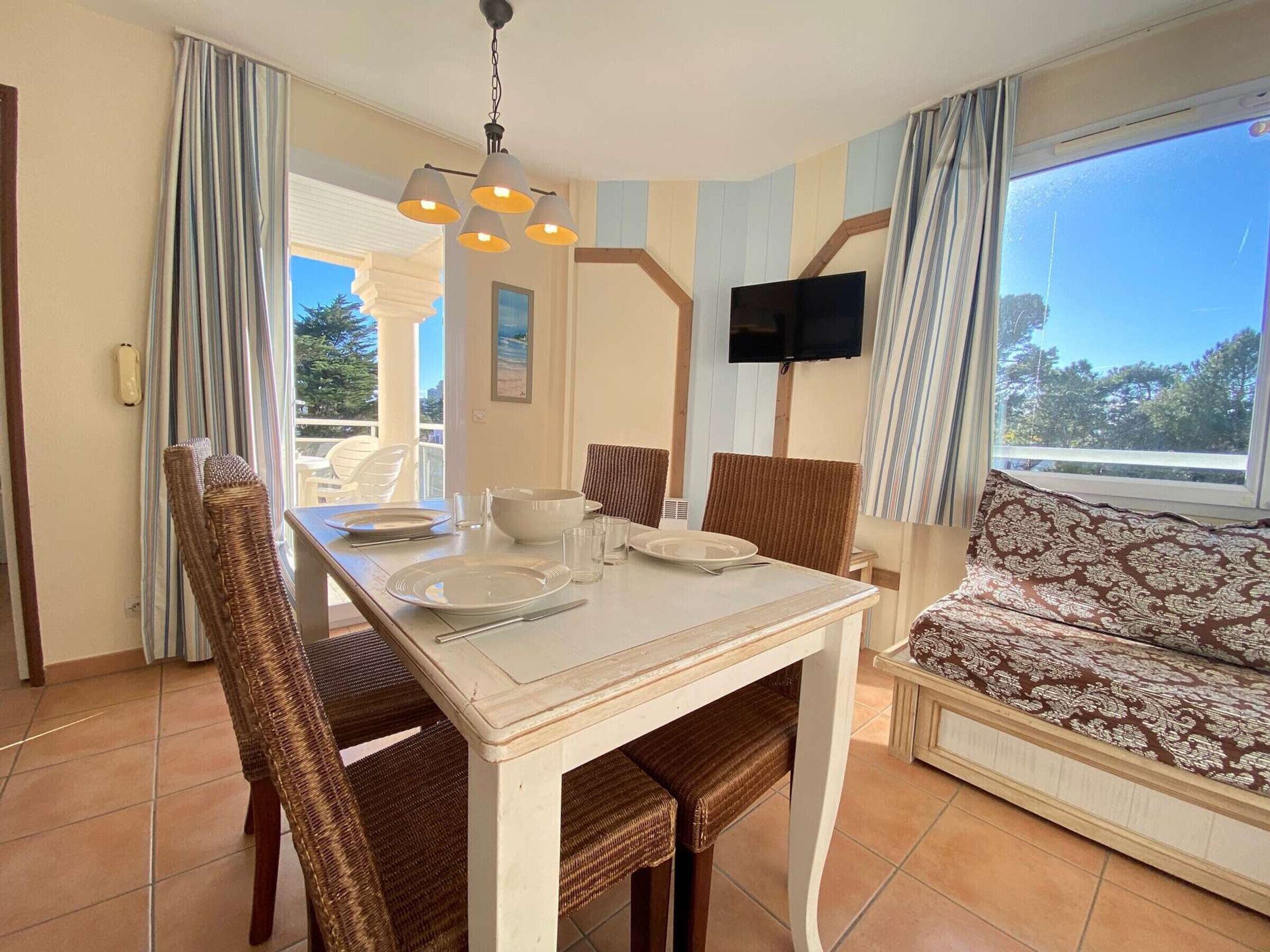 Un coin repas avec une table dressée pour deux personnes, un canapé et un téléviseur fixé au mur.