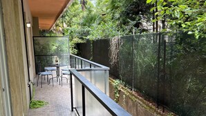 Ein Balkon mit Tisch und Stühlen, umgeben von üppiger Vegetation und einem Metallgeländer.