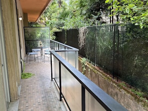 Ein Balkon mit Tisch und Stühlen, umgeben von üppiger Vegetation und einem Metallgeländer.