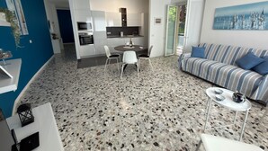 Ein modernes Wohnzimmer mit einem gestreiften Sofa, einem Esstisch mit Stühlen, einer Küchenzeile mit Mikrowelle und Backofen sowie einem großen Fenster.