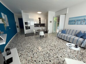 Ein modernes Wohnzimmer mit einem gestreiften Sofa, einem Esstisch mit Stühlen, einer Küchenzeile mit Mikrowelle und Backofen sowie einem großen Fenster.
