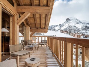 Ett trädäck med sittplatser, utsikt över snöklädda berg och en byggnad med trästomme.