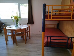 Ein Etagenbett mit einer roten Matratze, ein Holztisch mit Stühlen und ein Blumenvasen auf dem Tisch.