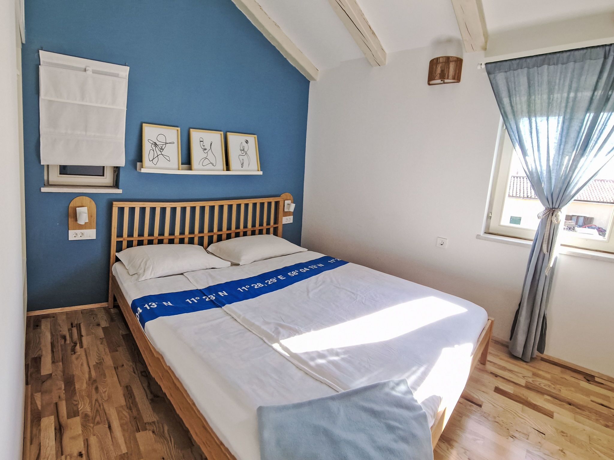 Een slaapkamer met een houten bed, een blauwe wand, een raam met gordijnen en lijstwerken aan de muur.