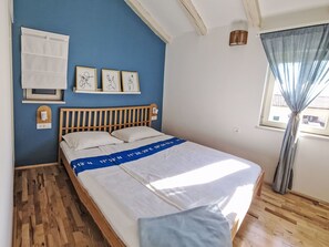 A bedroom with a wooden bed, a blue wall, a window with curtains, and framed artwork on the wall. - Apartment Ivas with balcony - A2 by Interhome (Umag/Zambratija)