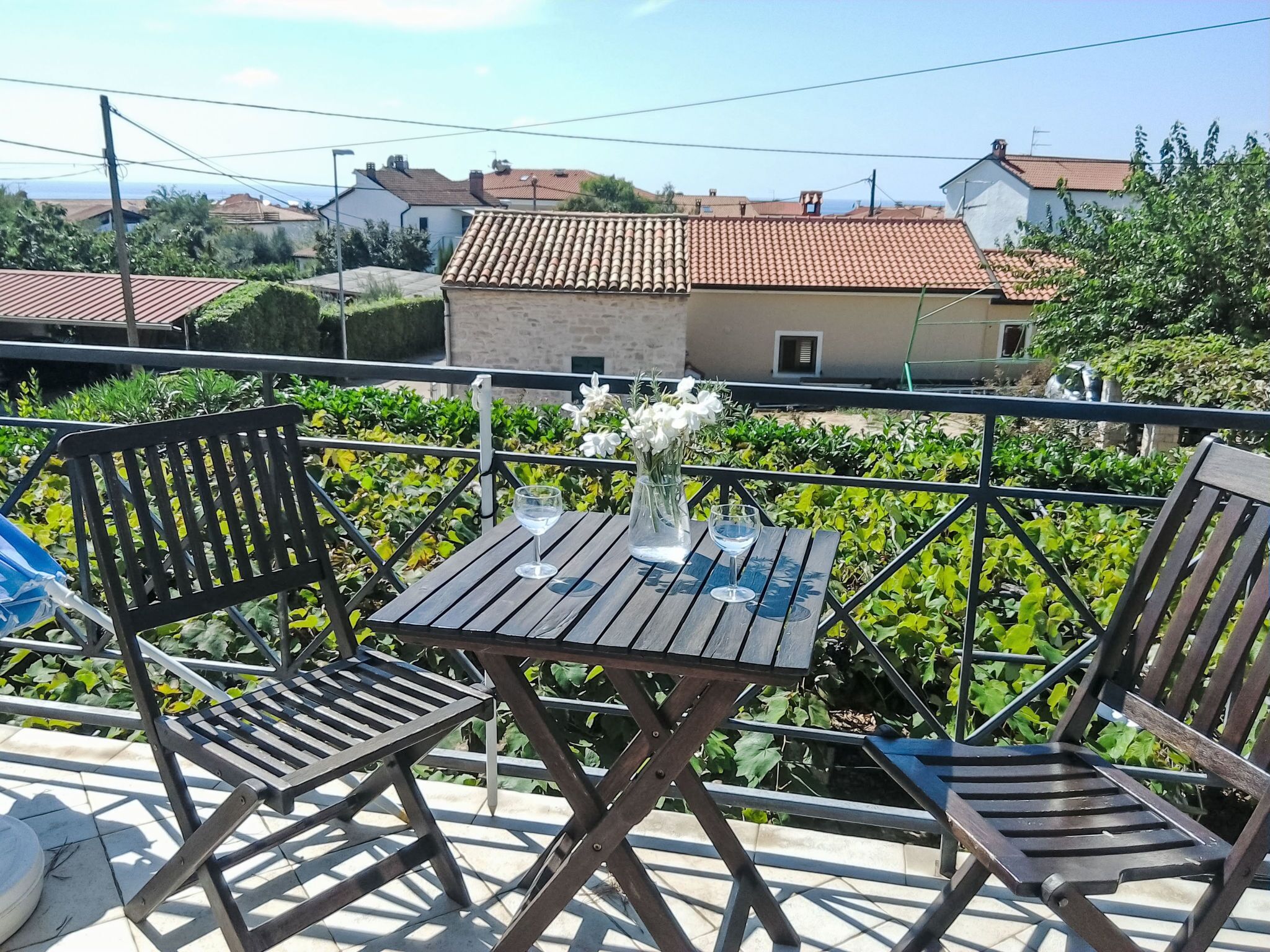 Un espacio al aire libre con una mesa y sillas, rodeado de vegetación y vistas a un barrio residencial.