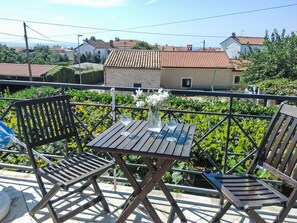 Ein Sitzbereich im Freien mit Tisch und Stühlen, umgeben von Grünpflanzen und mit Blick auf eine Wohngegend.