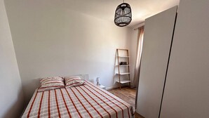 Un dormitorio con cama, mesita de noche, lámpara, armario y estantería escalonada.
