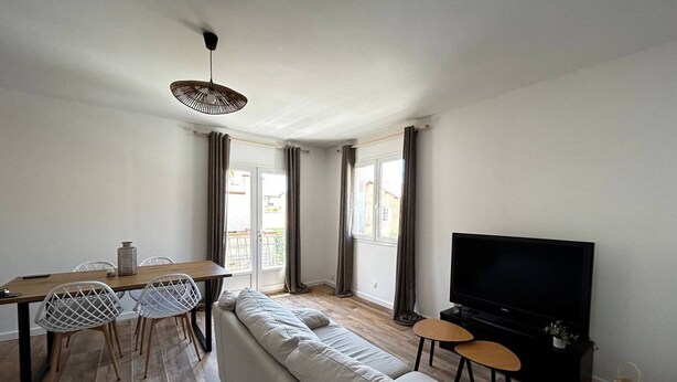 Un salón moderno con sofá, televisor, mesa de comedor, sillas y vistas al balcón.