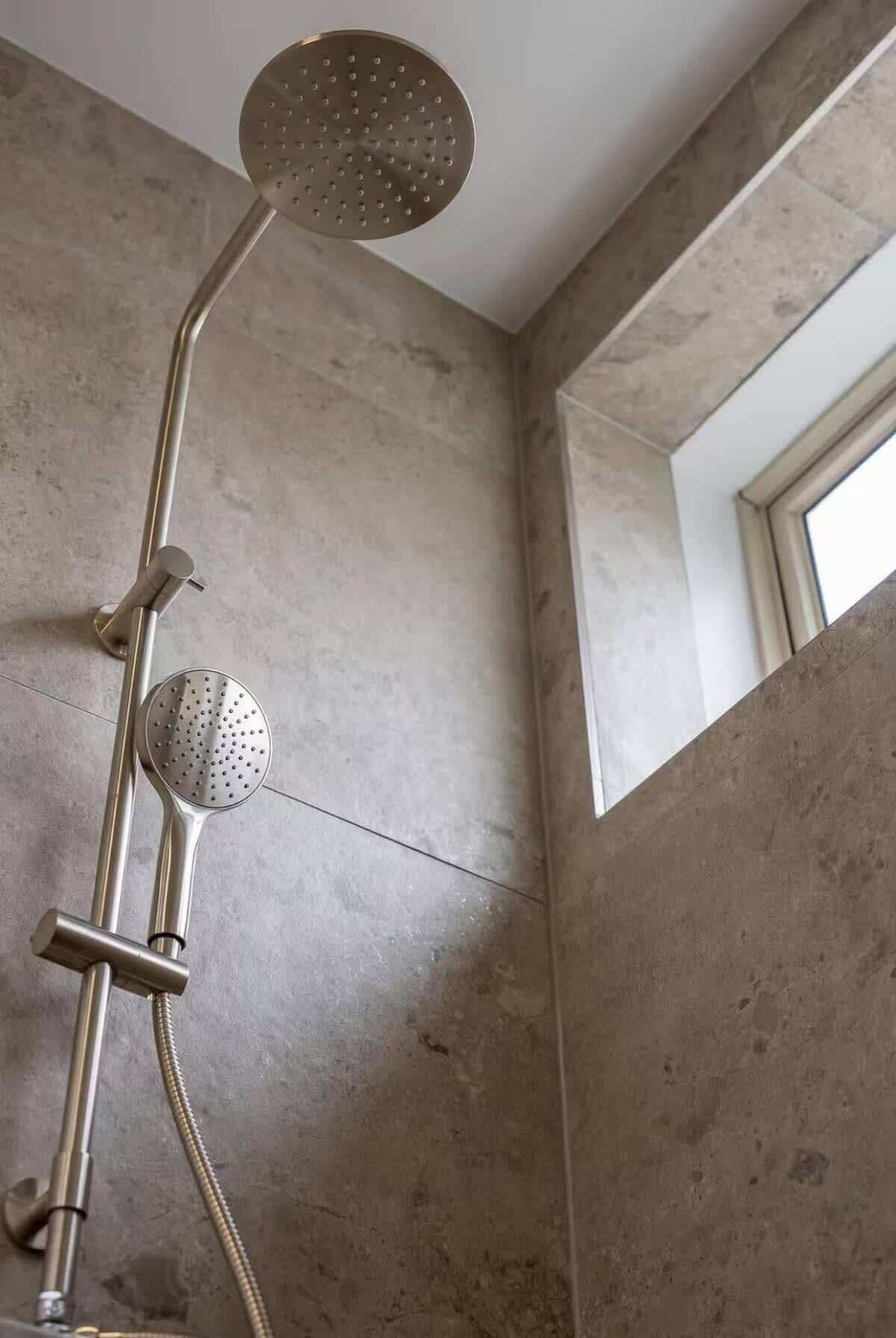 Une douche équipée d’un pommeau de douche à main et d’un pommeau de douche fixe, tous deux fixés au mur.