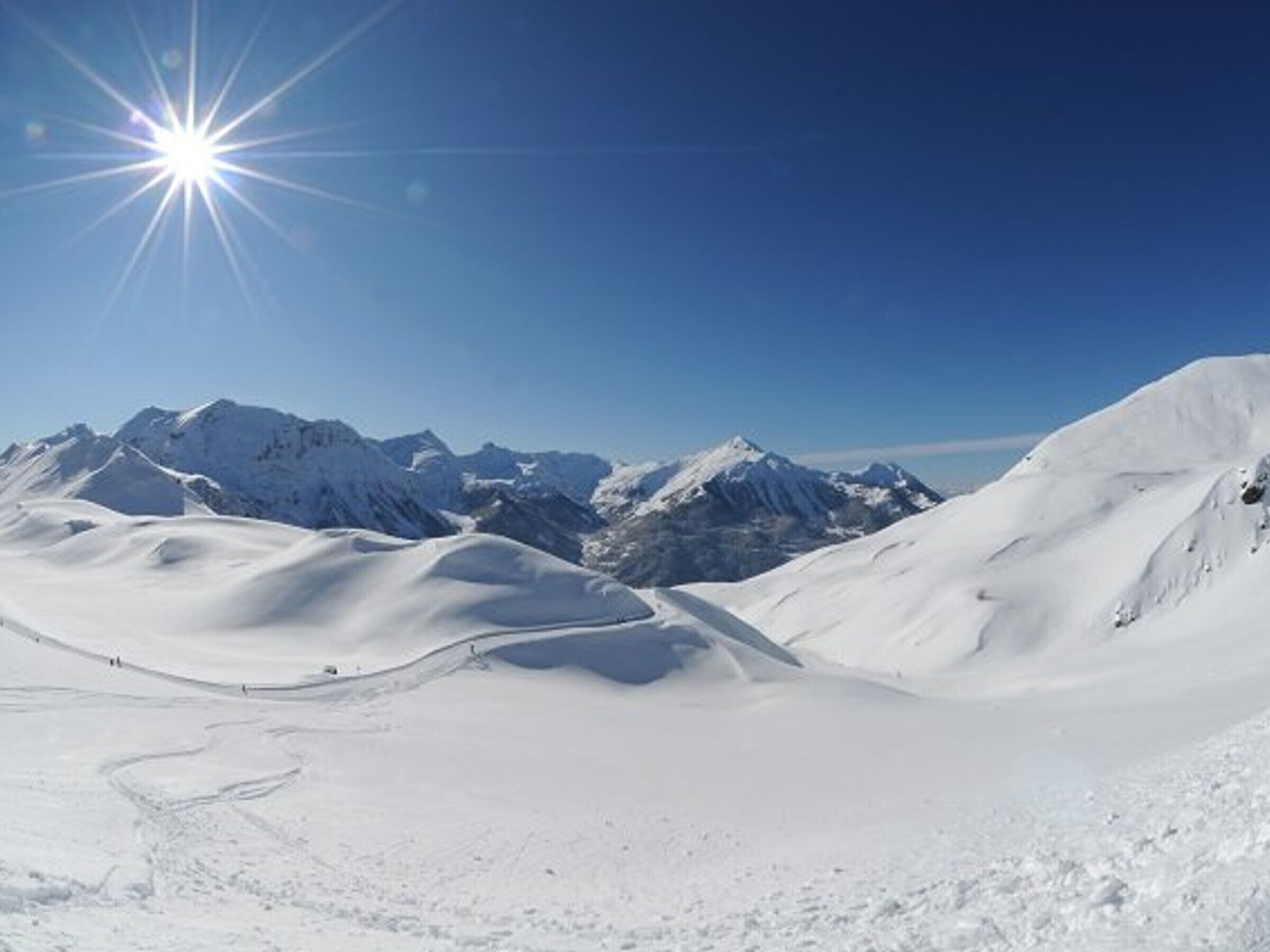 Een berglandschap bedekt met sneeuw, heldere luchten en een felle zon.
