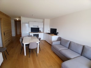 Ein kompakter Wohnraum mit Küchenzeile, einer Essecke mit Tisch und Stühlen sowie einem grauen Sofa.