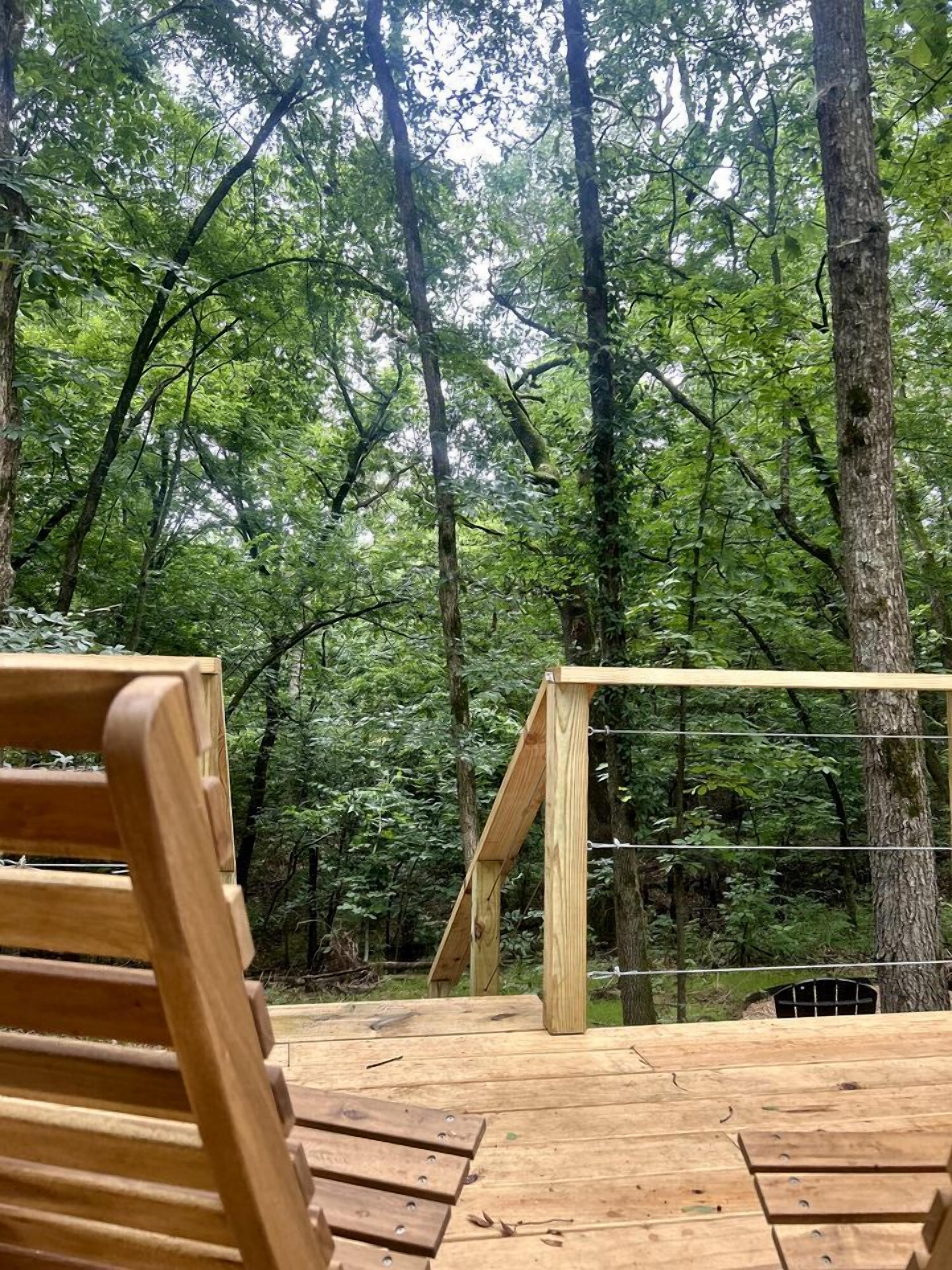 A wooden deck with a wooden chair, surrounded by a forest with tall trees.