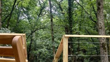 A wooden deck with a wooden chair, surrounded by a forest with tall trees.