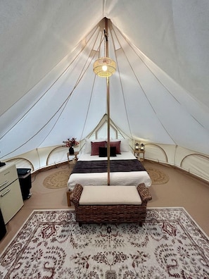 Une tente équipée d’un lit, d’une lampe, d’une petite table et d’une chaise.