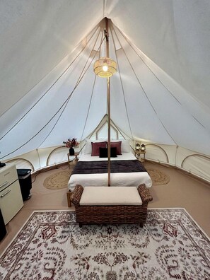 A tent with a bed, a lamp, a small table, and a chair.