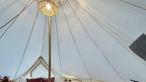 A tented accommodation with a bed, a wicker bench, a hanging light fixture, and a patterned rug.