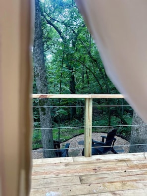 A wooden deck with a rope barrier, a chair, and a view of a forested area. - Mt. Magazine Tent (Gentry)