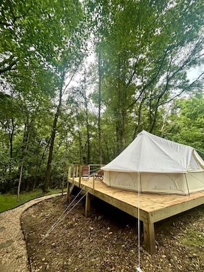Une tente blanche, montée sur une plateforme en bois, au cœur d’une forêt.