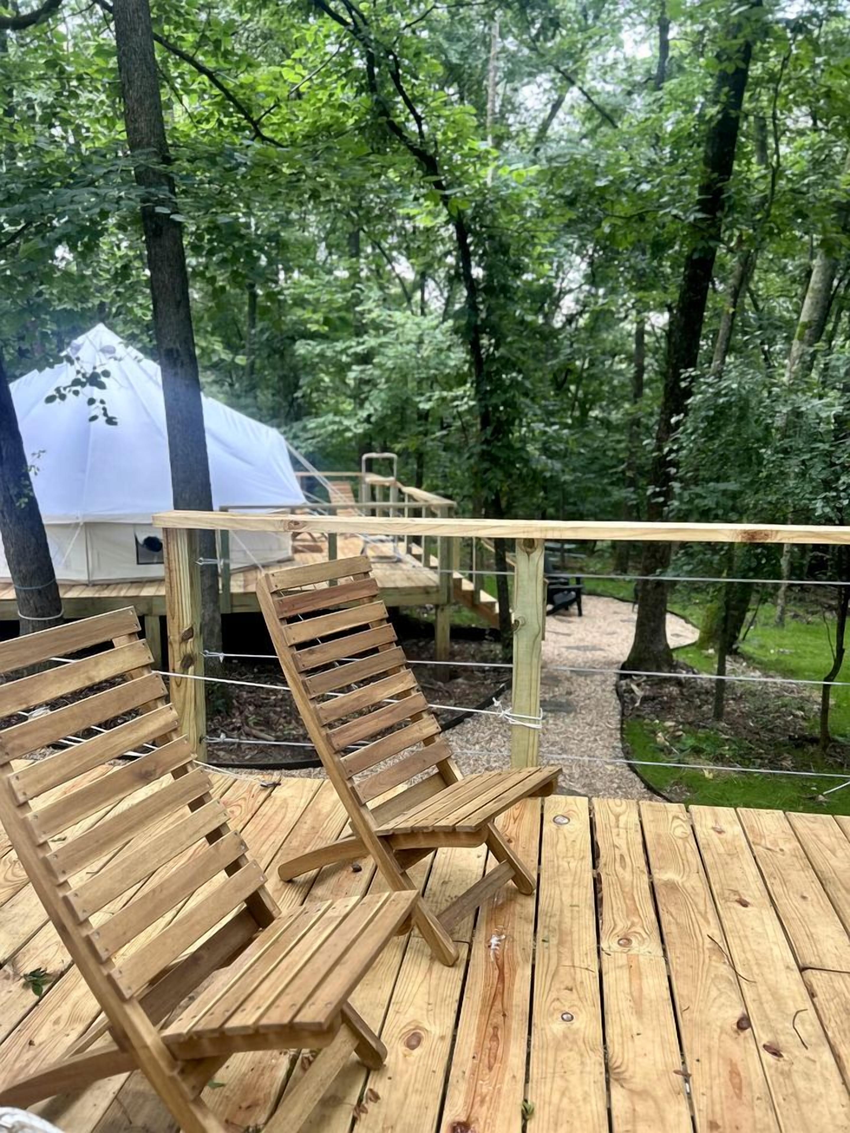 A wooden deck with two wooden chairs, a white tent, and a wooden staircase leading to a higher platform.
