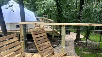 A wooden deck with two wooden chairs, a white tent, and a wooden staircase leading to a higher platform.