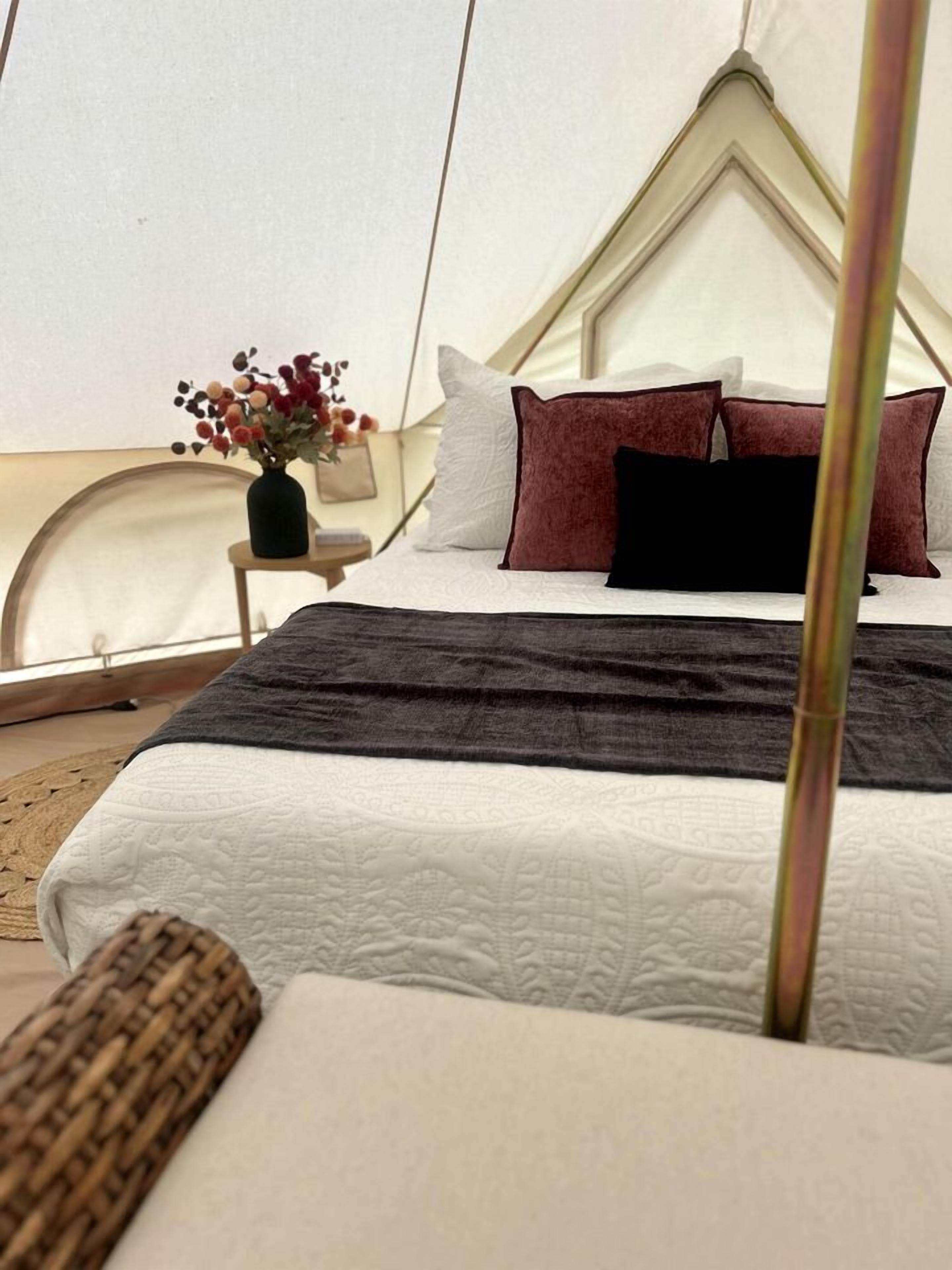 A tent-style room with a bed, pillows, a bedside table, and a vase with flowers.